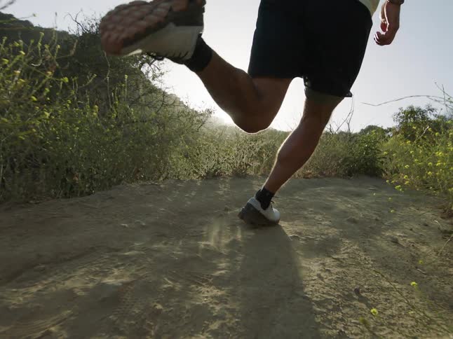 A man runs on a dirt path through a grassy plain
