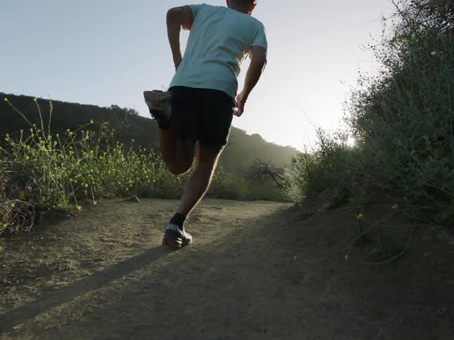 Man running down a trail with the sun on the horizon