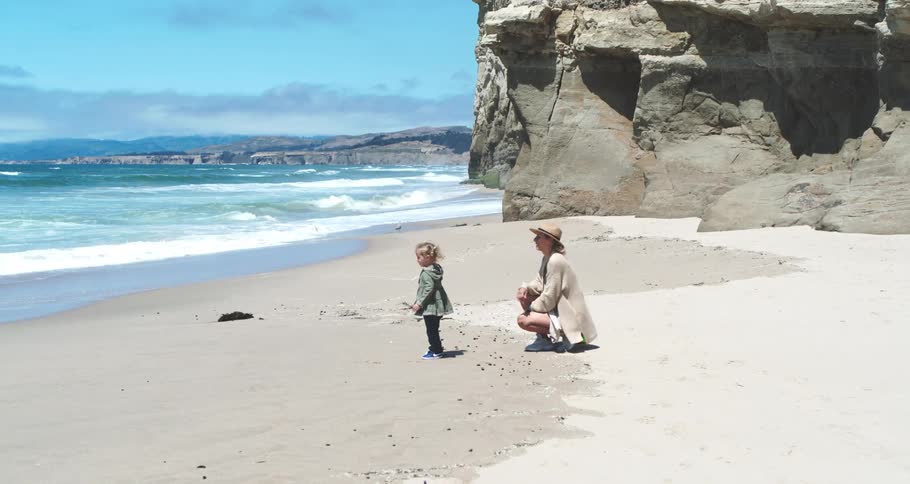 A mother and young daughter are on the beach throwing rocks into the ocean