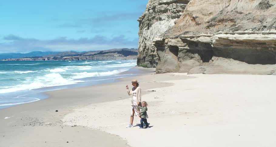 Mother holding hands with her son walking on the sand at the beach