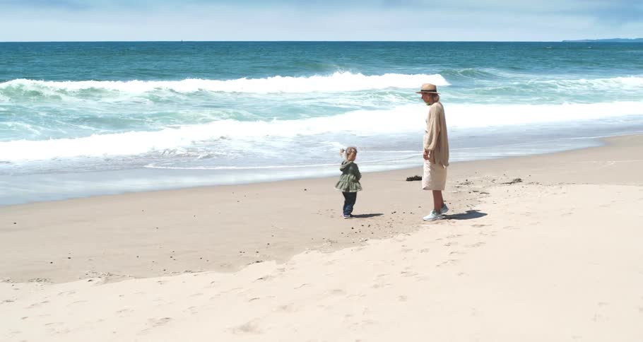 A mother and her daughter playing on a sandy beach with waves rolling in from the sea on a sunny day