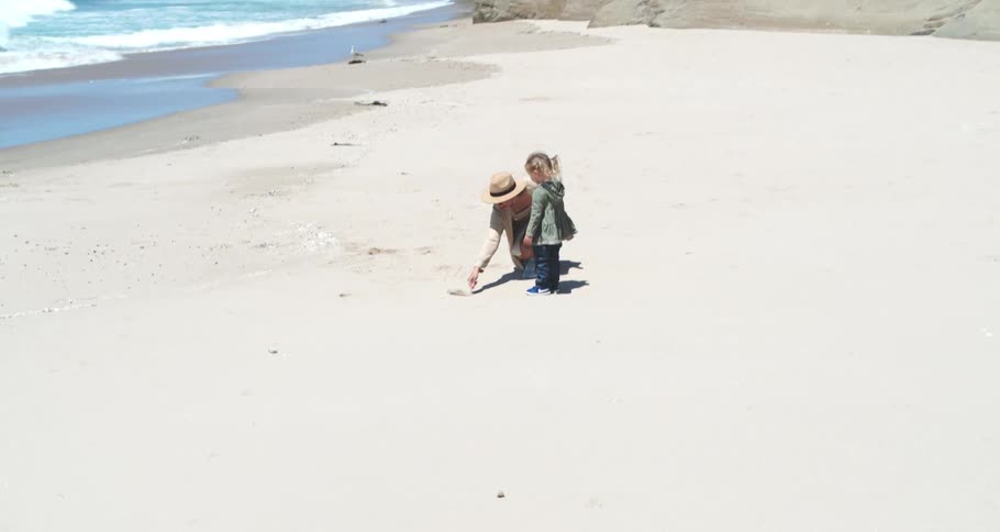 Mother playing with her little daughter in the sand on the beach