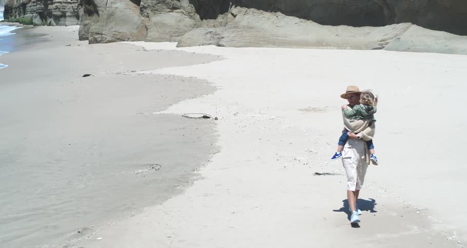 Mother with her little daughter in her arms walking on the sand at the beach