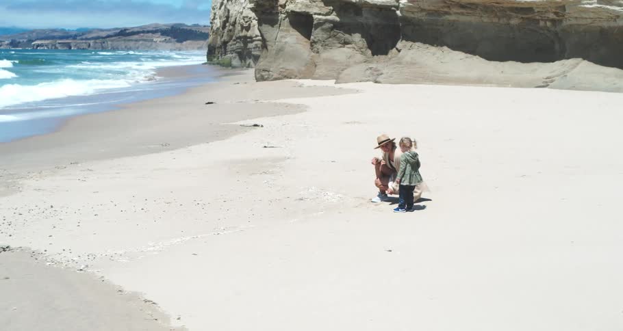 A mother draws in the sand with her finger while her daughter watches