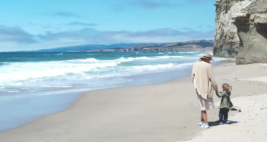 Mother holding hands with her daughter walking on the sand at the beach