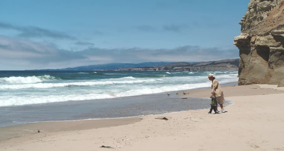 A mother and her son walk backwards on a beach to avoid the incoming tide