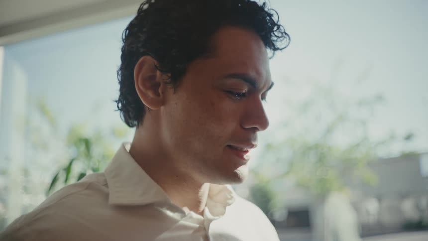 Man stands near the window in a sunlit office frowning while thinking