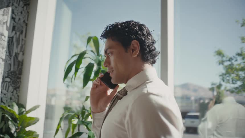 A man in a white shirt and tie smiling while talking on a phone