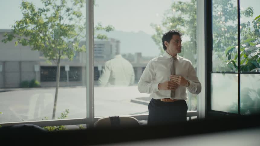 Office worker neatens himself while standing in a meeting room as traffic passes in the background