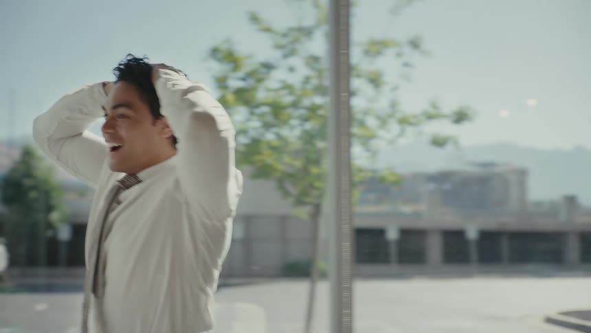 A man wearing office attire celebrates by putting his hands to his head and stomping around with a huge smile