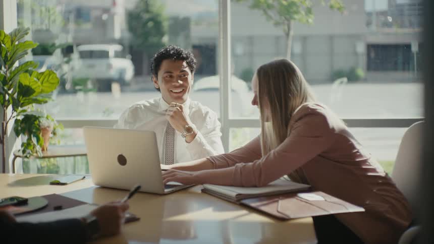 Office worker in a meeting leans over to type on coworkers laptop