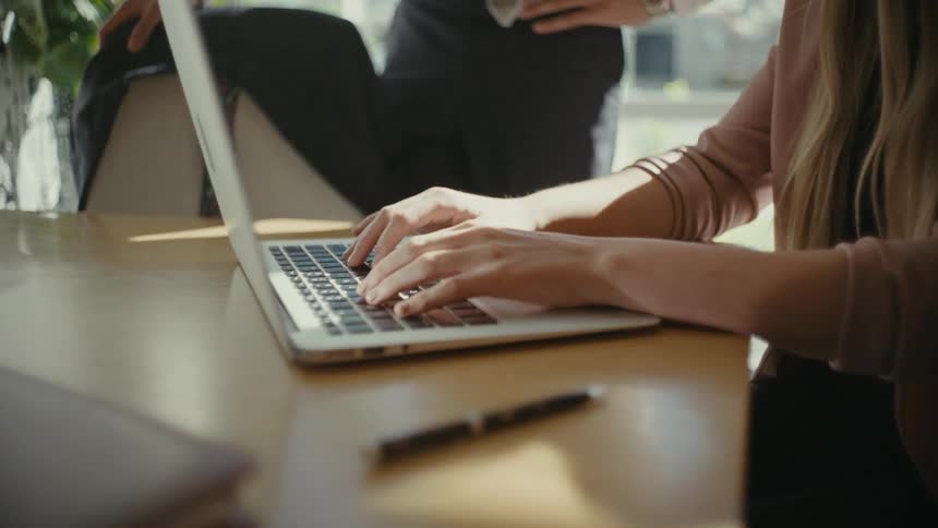 Hands of a woman typing on a laptop on top of an office desk
