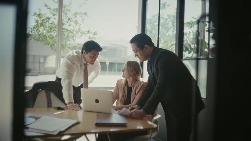 Three people in an office room talking with a laptop