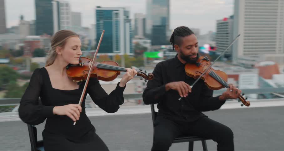 Man and woman sitting on a chair on the terrace of a building playing the violin