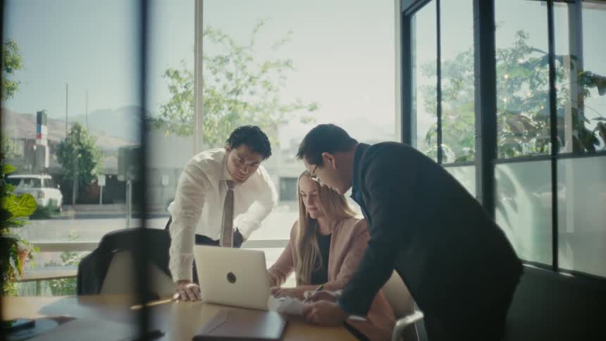 Woman sitting at an office desk with two men around her talking