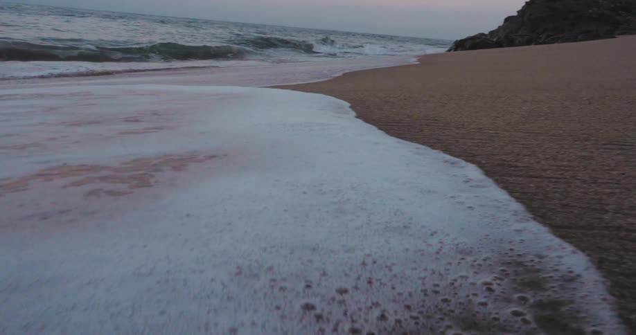 A tranquil beach at twilight with gentle waves lapping against the sandy shore
