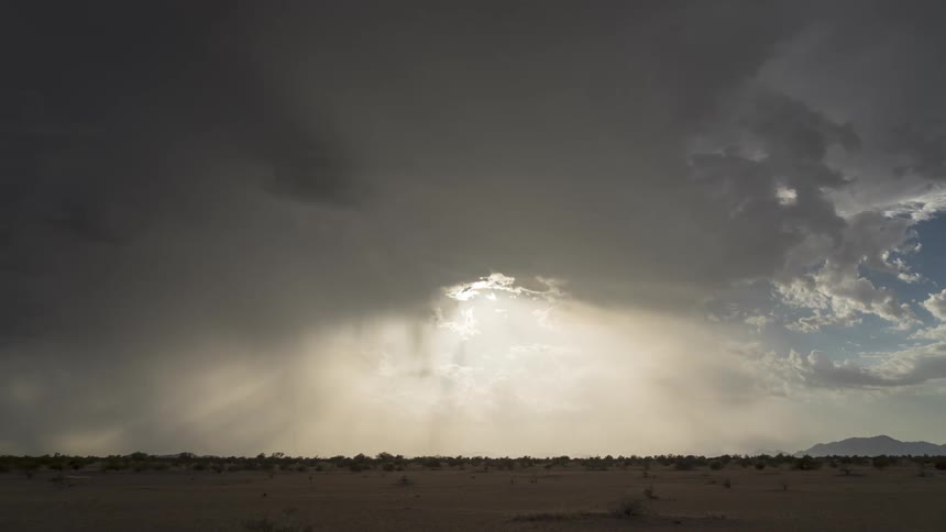 Sunlight pierces through dark clouds illuminating a vast desert landscape under a stormy sky