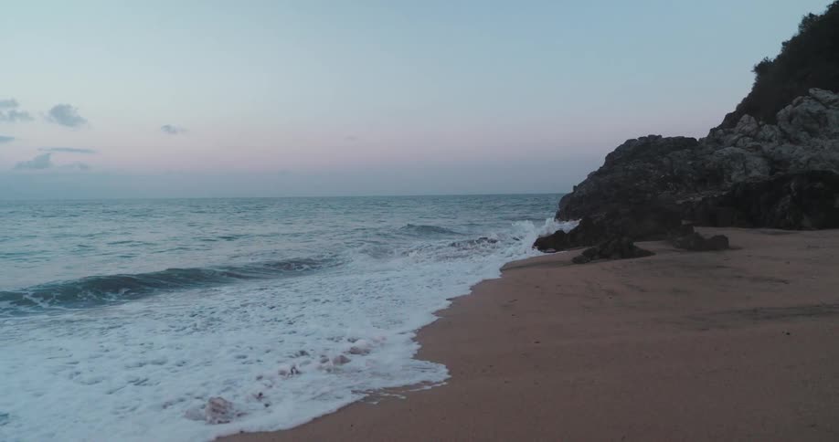 A tranquil beach at twilight with gentle waves washing ashore with a rocky outcrop on the right side of the beach