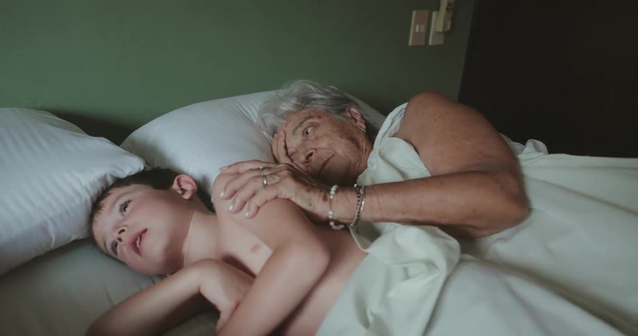 Grandmother lying down with her grandson cuddling him