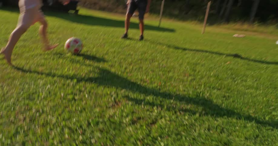 Boy playing soccer on a grass field with his grandfather and kicking a ball into the goal