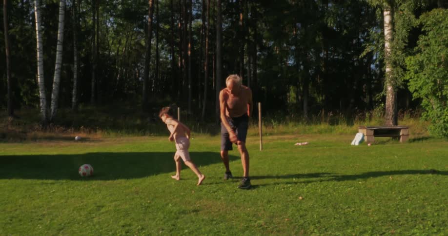Boy playing soccer on a grass field with his grandfather