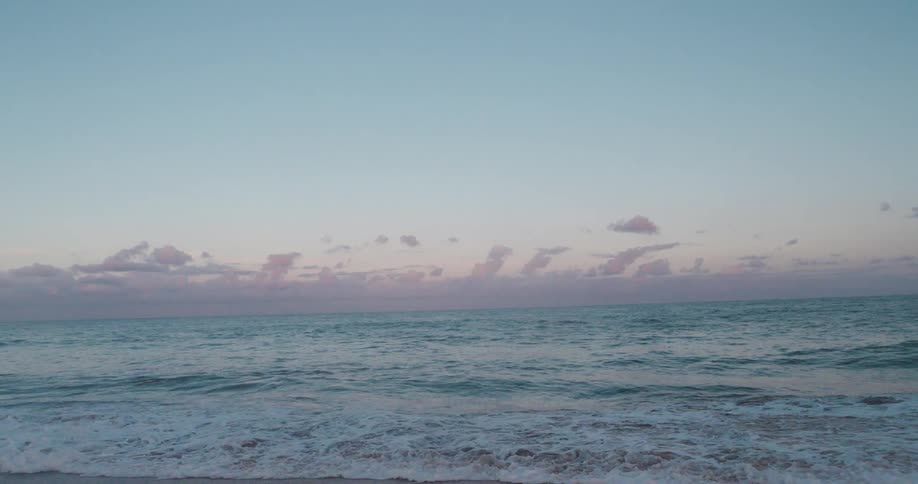 A serene beach scene with gentle waves lapping onto the shore under a dusky sky dotted with clouds