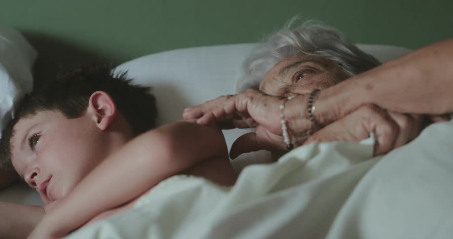 Grandmother lying in bed with her grandson stroking his arm