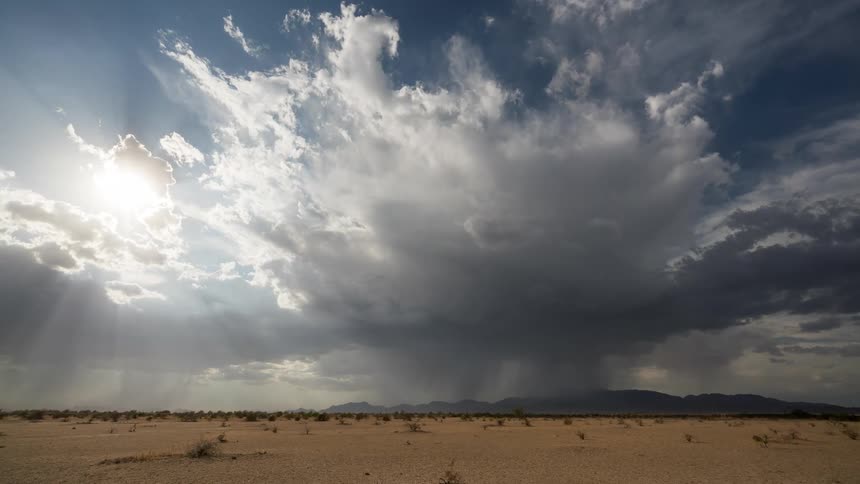 Heavy stormy clouds passing over a desert landscape with mountains on the horizon