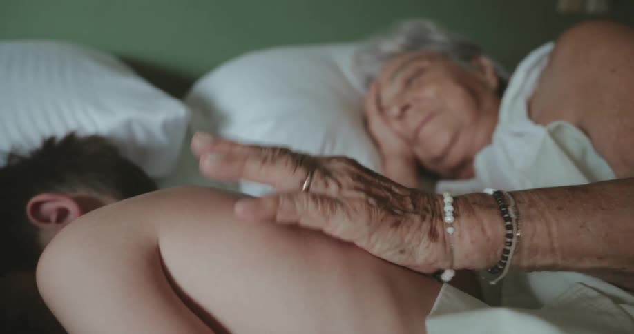 Grandmother comforts her grandson while they lie on a bed
