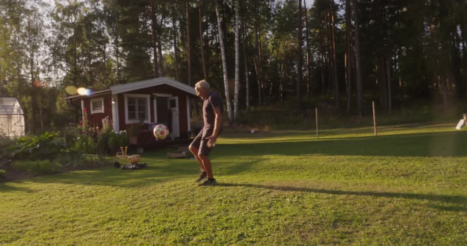Elder man in a grassy yard doing keepieuppies with a ball