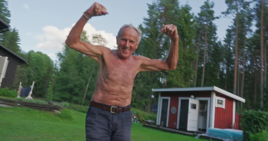 Shirtless elderly man raising his hands while standing in a backyard garden of a house