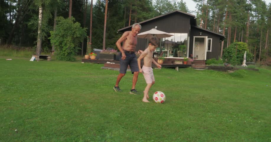 Boy playing soccer in the grassy backyard with his grandfather