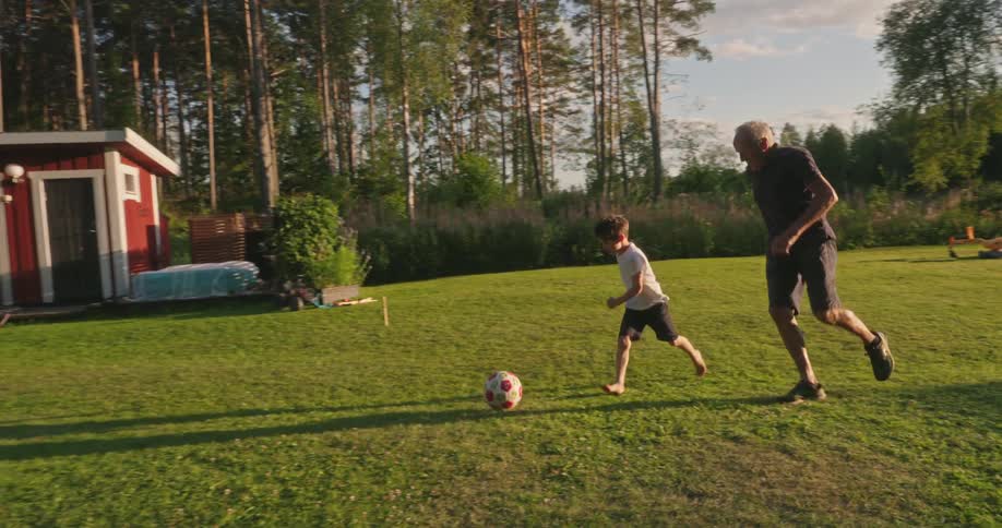 Grandad playing ball with his grandson in the grassy backyard