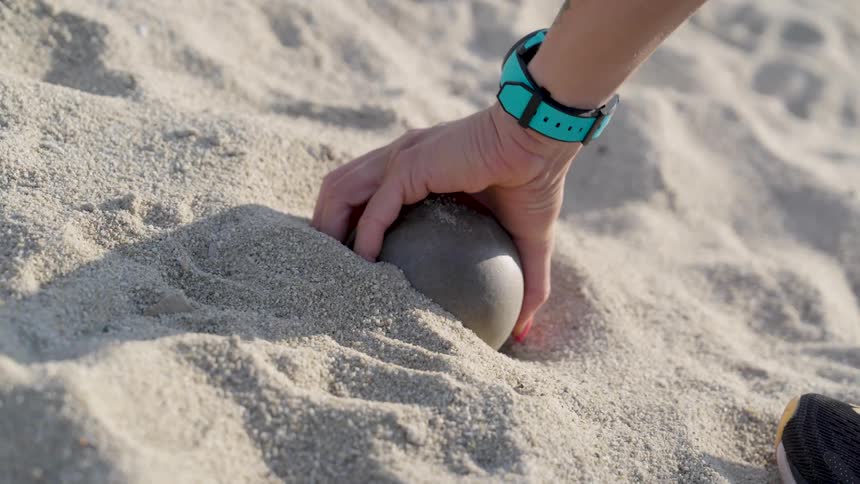 Close up of a hand picking a small ball from a ground on a sandy beach