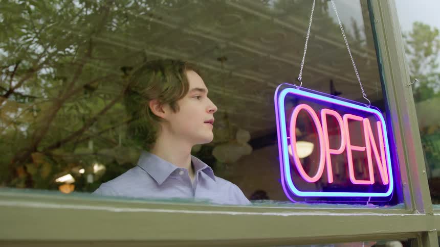 Man turning on neon sign that says open in a store window