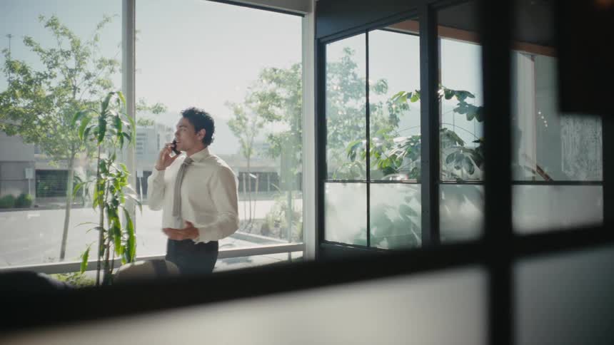 A man wearing business attire talking on his smartphone from a modern office
