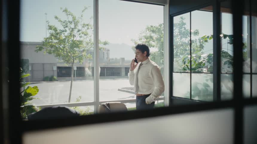 A man wearing business attire talking on his smartphone from a modern office