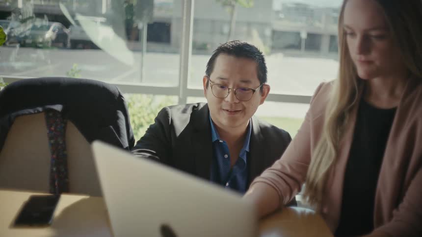 Two individuals engaged in a discussion at a table while looking at a laptop