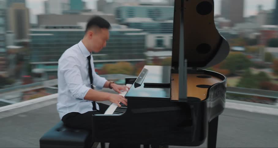Man plays a baby grand piano on the roof of a building in the city