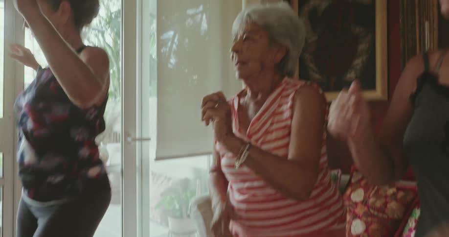 Three women exercise together by dancing together in a living room