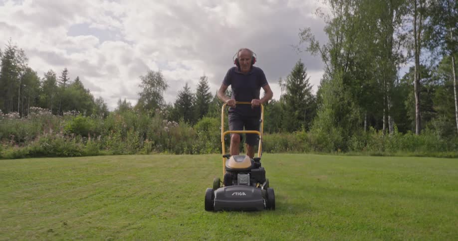 Man cutting grass in a large garden with trees around