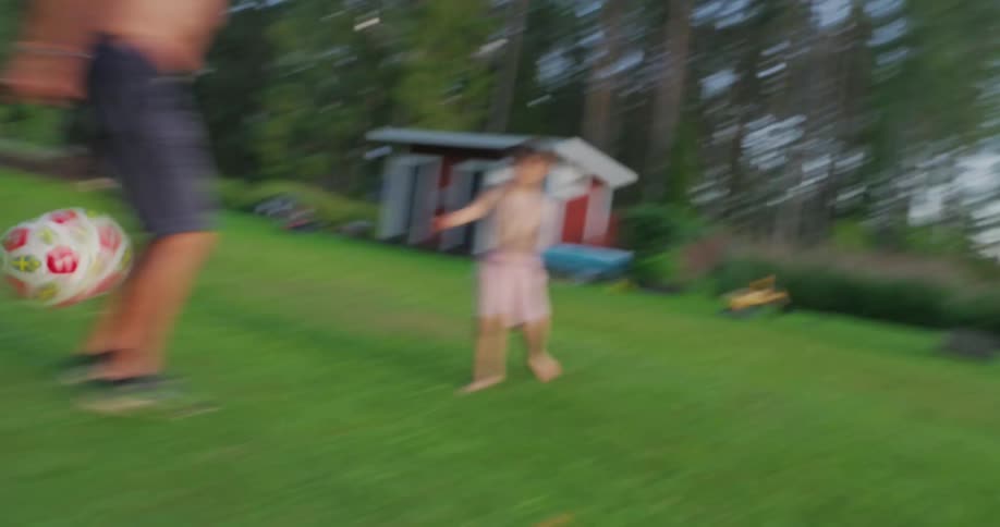 A child and an adult playing with a soccer ball on a grassy field during daytime under clear skies
