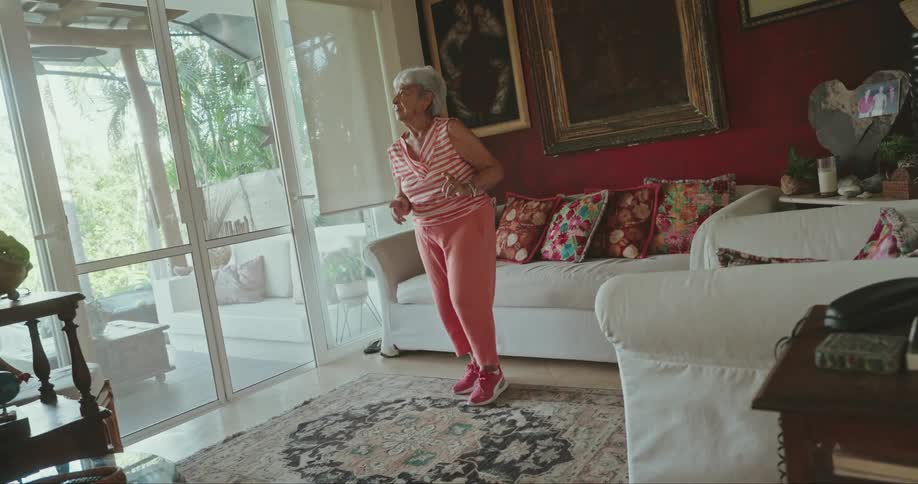 An elderly woman in workout attire dancing in a welllit living room