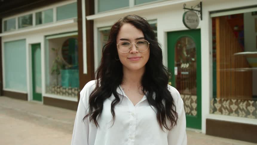 Smiling woman stands on the sidewalk near a store