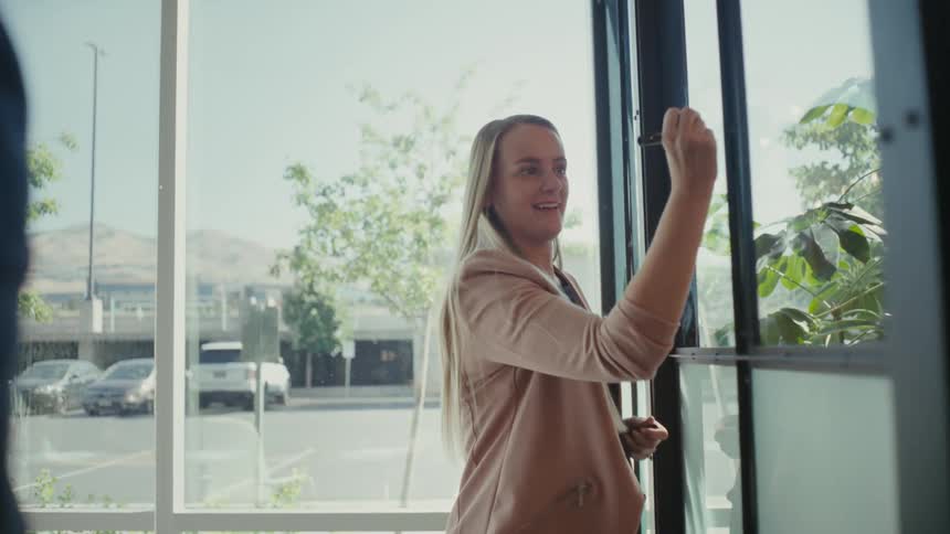 Cheerful blonde woman standing writing on glass in an office