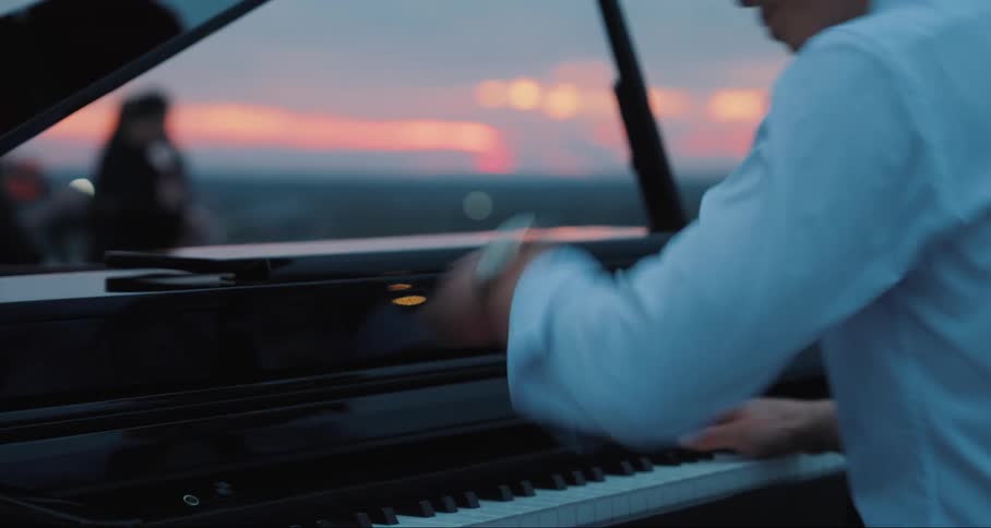 Man playing piano and in the background women playing violin at sunset