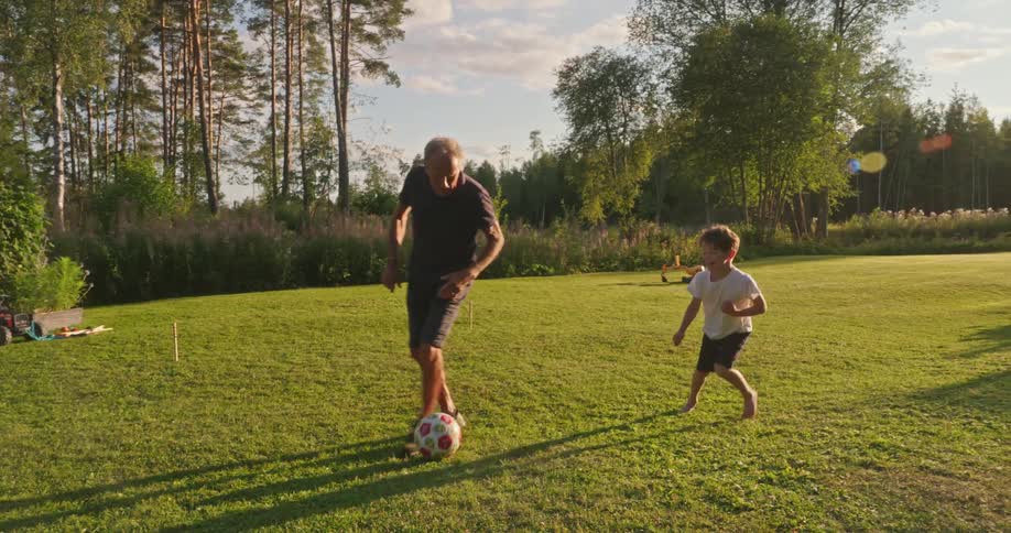 Elderly man playing ball with a boy in a grassy yard