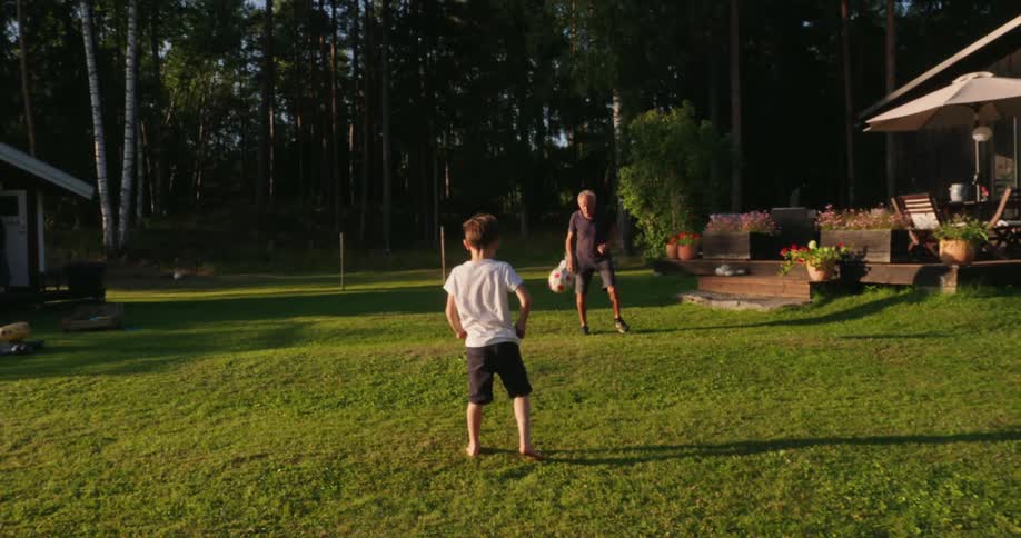Boy playing soccer in the backyard of a house with his grandfather
