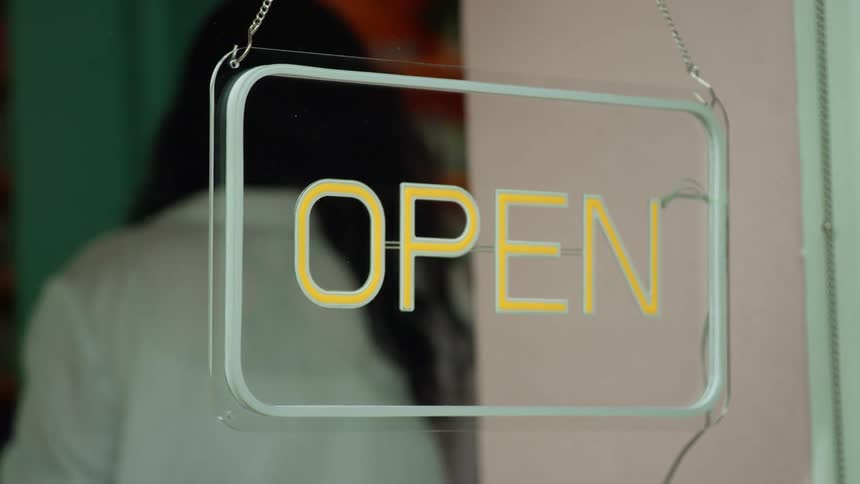 A woman turns off the open sign hanging in her shop window