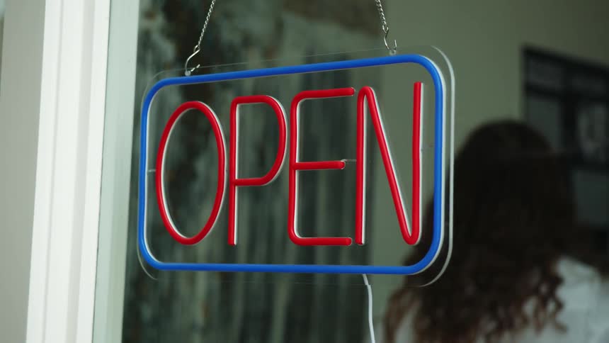 Woman hanging up an open sign on a glass window in a store